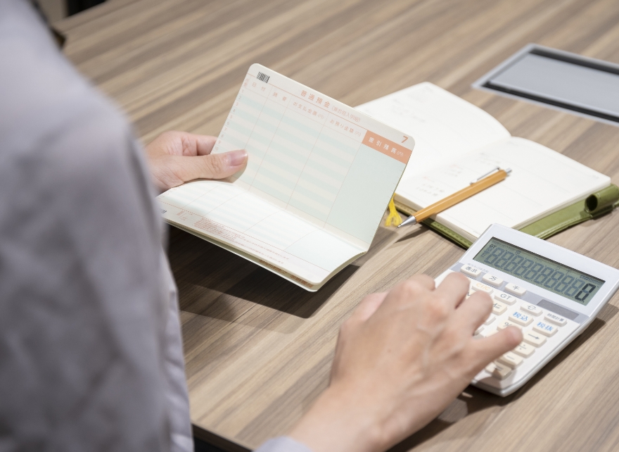 通帳を広げながら電卓を使って計算する手元