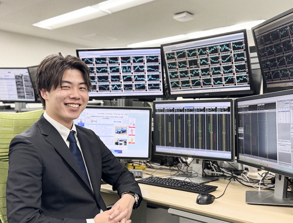 マルチモニターの前で微笑む男性ディーラー